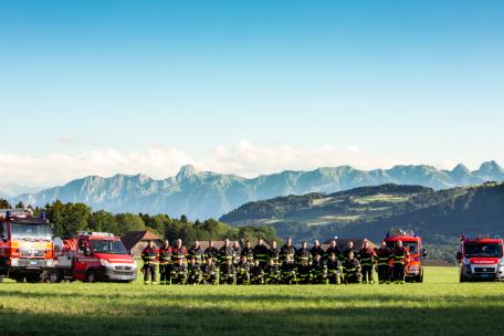 Team Feuerwehr mit Fahrzeugen auf Wiese mit Bergen im Hintergrund